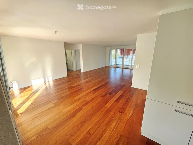 Empty room with wooden flooring and white walls, featuring large sliding glass doors leading to a balcony.