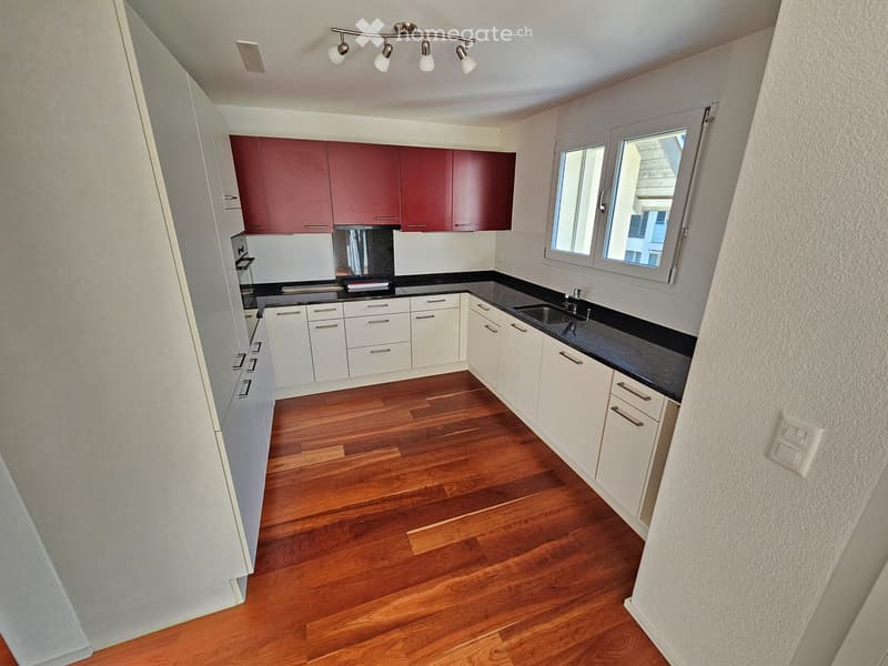 Modern kitchen with white and red cabinets, wooden flooring, and a black countertop.
