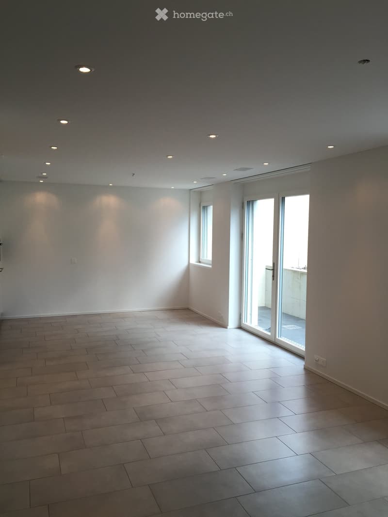 Empty room with tiled floor, white walls, recessed ceiling lights, and large sliding glass doors leading to a balcony.