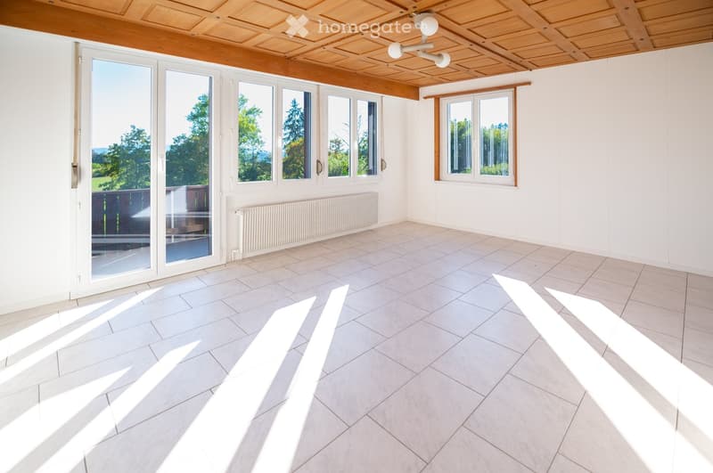 Empty room with white walls, tiled floor, large windows, and a sliding glass door leading to an outdoor area.