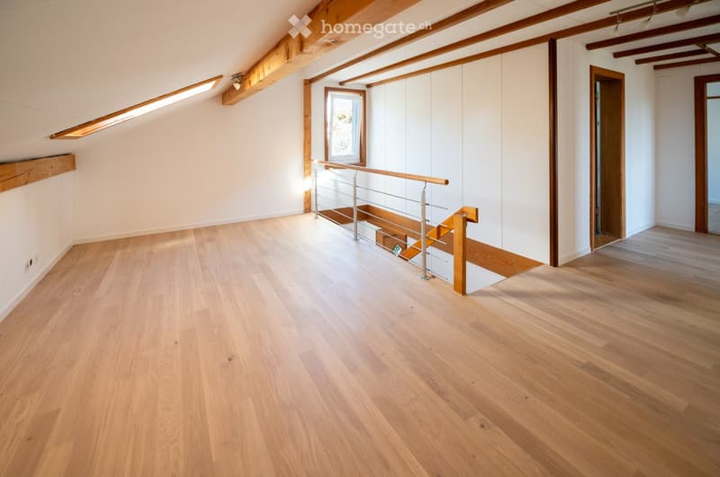 Empty room with wooden flooring, white walls, exposed wooden beams, and a staircase leading to another level.