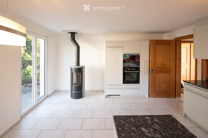 Modern kitchen with white cabinets, a wood stove, and an oven, featuring large windows and a tiled floor.