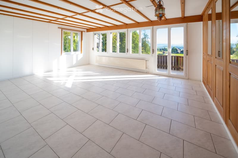 Bright, empty room with white tiled floor, large windows, wooden ceiling beams, and a radiator. No furniture or equipment present.