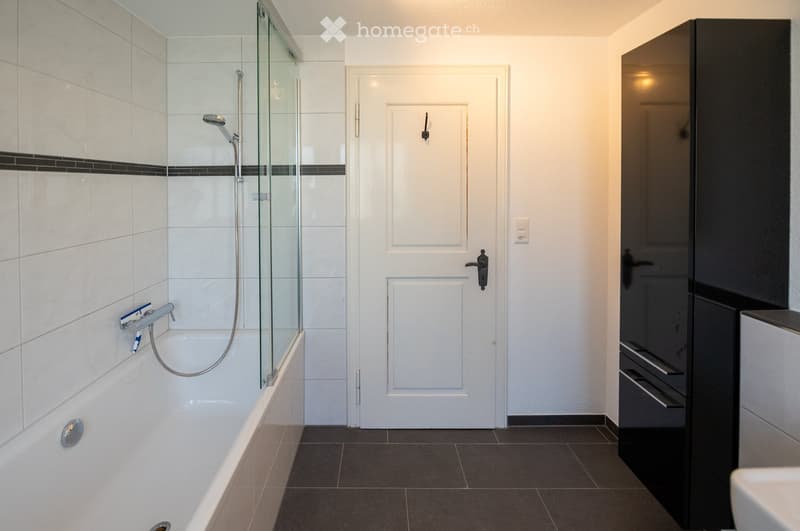 Modern bathroom with a white bathtub, glass-enclosed shower, and sleek black cabinetry.