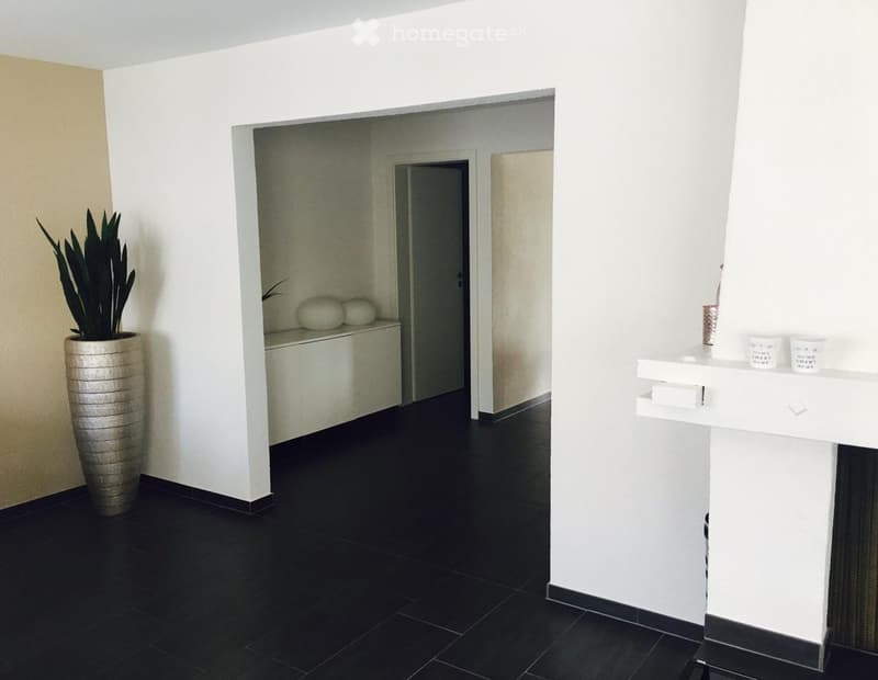 Modern hallway with black tiled floor, white walls, a tall vase with a plant, a small shelf with decorative items, and a white console table with cups and a small decorative item.