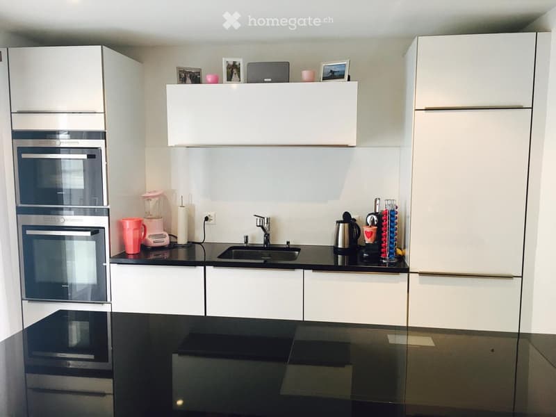 Modern kitchen with white cabinets, black countertops, stainless steel appliances, and various kitchen items on the counter.