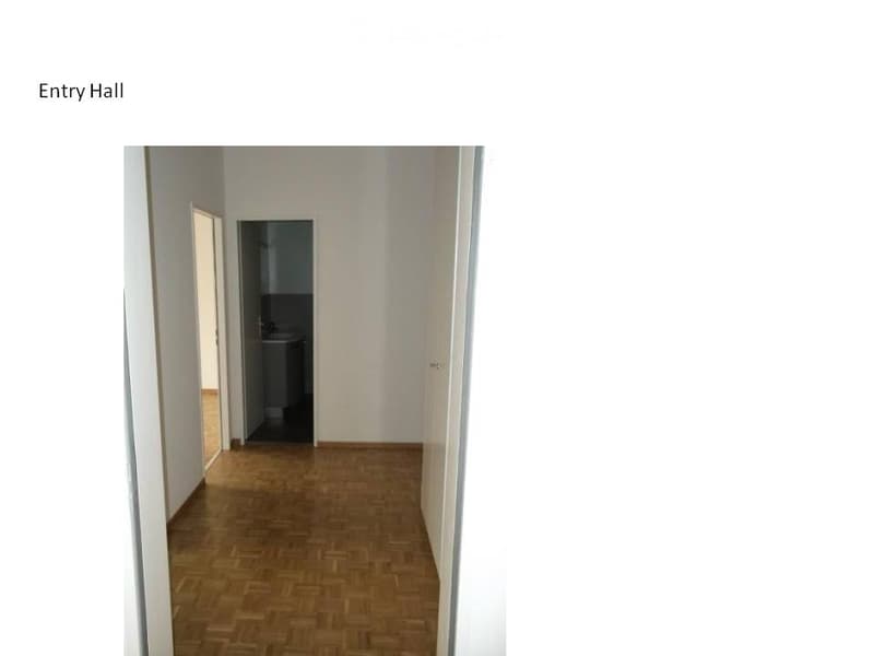 Empty entry hallway with wooden flooring and white walls, leading to a small bathroom area.