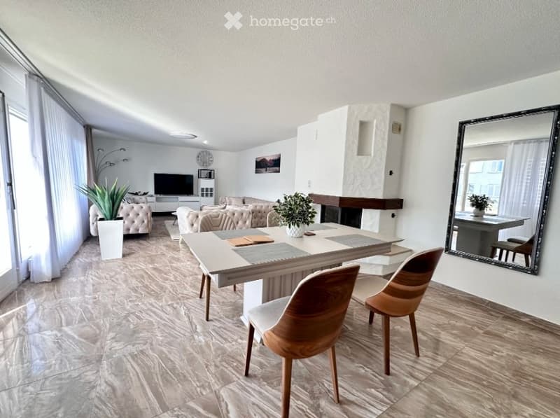 Modern living room with a large window, marble flooring, a sofa, coffee table, dining table with chairs, and a fireplace area.