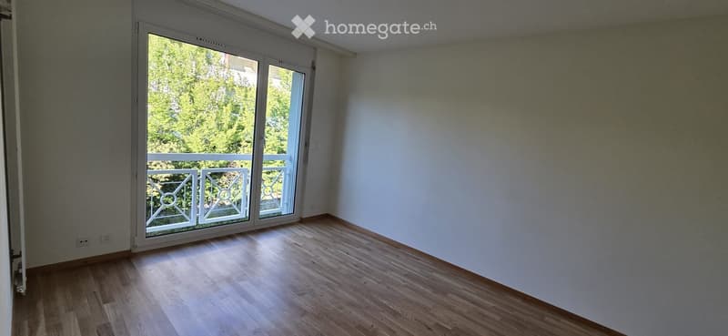 Empty room with wooden flooring, white walls, and large sliding glass doors leading to a balcony with a metal railing.