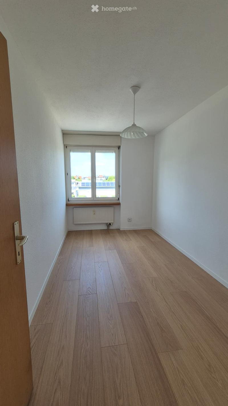 Empty room with wooden flooring, white walls, a window with blinds, a radiator, and a hanging light fixture.