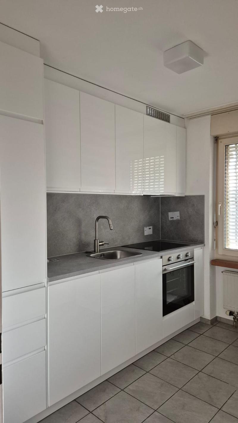 Modern kitchen with white cabinets, stainless steel sink, faucet, and built-in oven. Grey tiled backsplash and countertop.