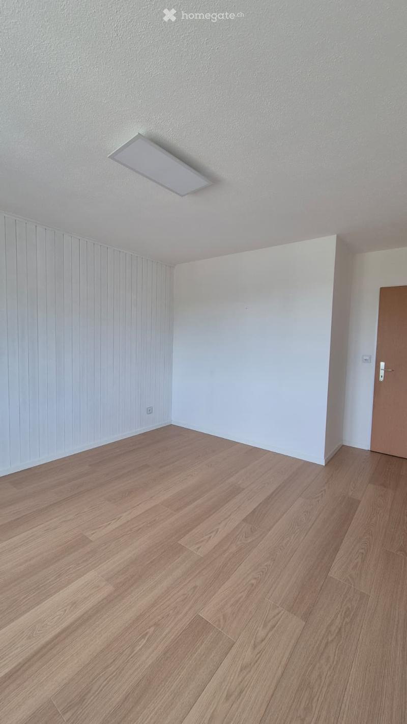 Empty room with light wooden flooring, white walls, and a single door.