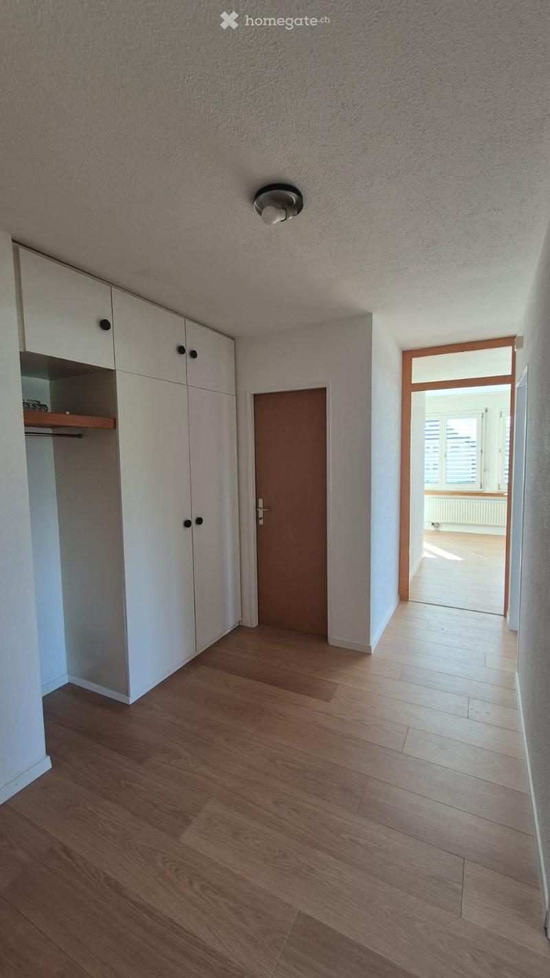 Empty hallway with wooden flooring, white walls, built-in white closet with shelves, and a closed door leading to another room.
