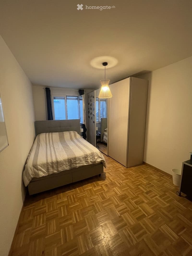 Bedroom with wooden herringbone flooring, a grey bed with striped bedding, a tall wardrobe, and a hanging pendant light fixture.