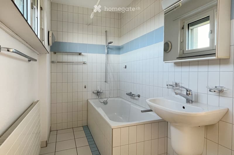 Bathroom with white tiled walls, a bathtub, a sink, a mirror, and a showerhead. The walls have a blue accent stripe near the top.