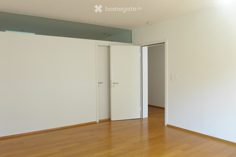 Empty room with white walls, wooden floor, and two white doors leading to adjacent spaces.