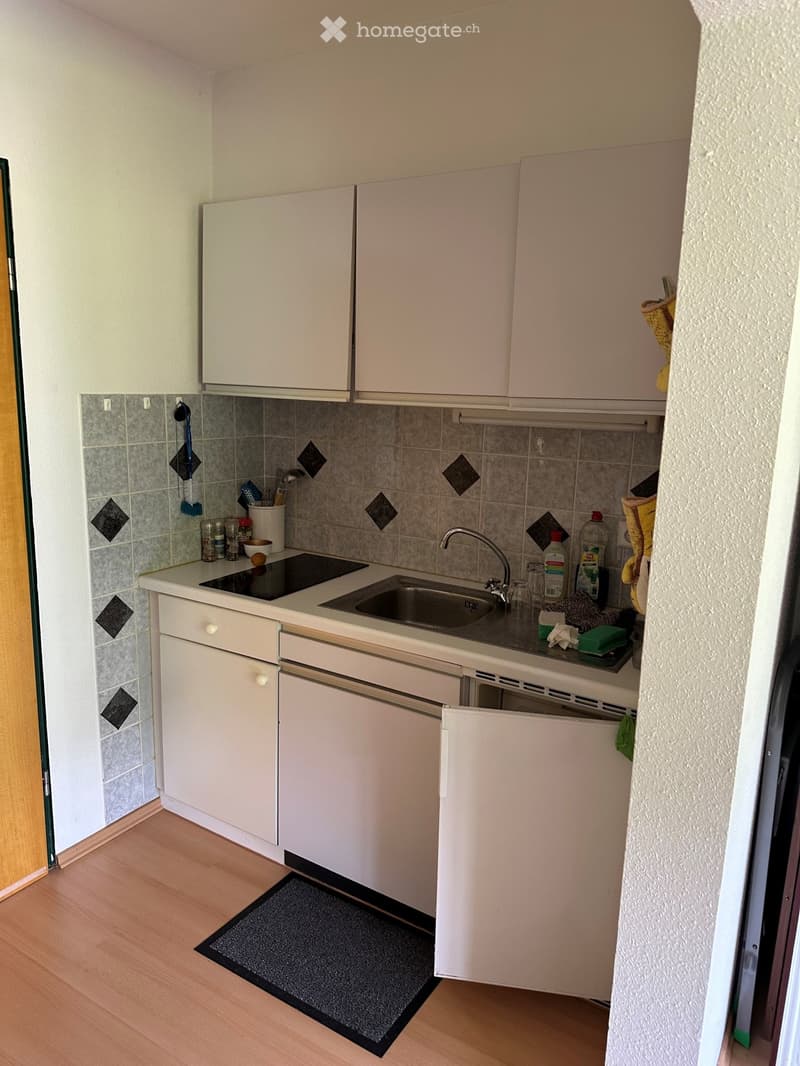 Compact kitchen with white cabinets, a sink, electric stove, and various small appliances and utensils on the counter.