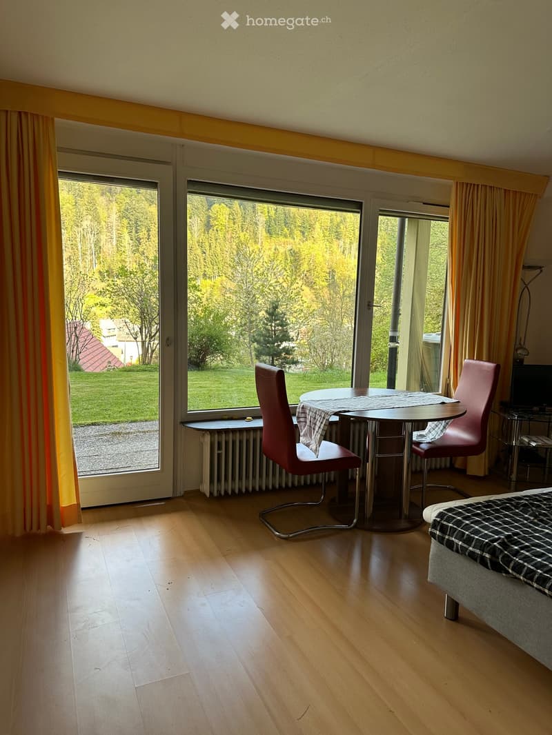 Living room with large sliding windows, wooden floor, table and chairs, and a view of a mountain landscape