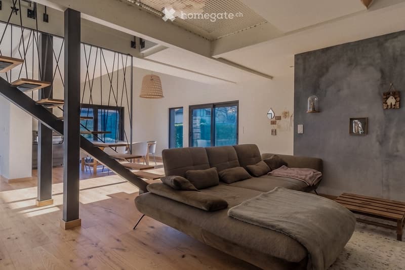 Modern living room with a large sectional sofa, ottoman, dining table, chairs, and a staircase leading to an upper level.