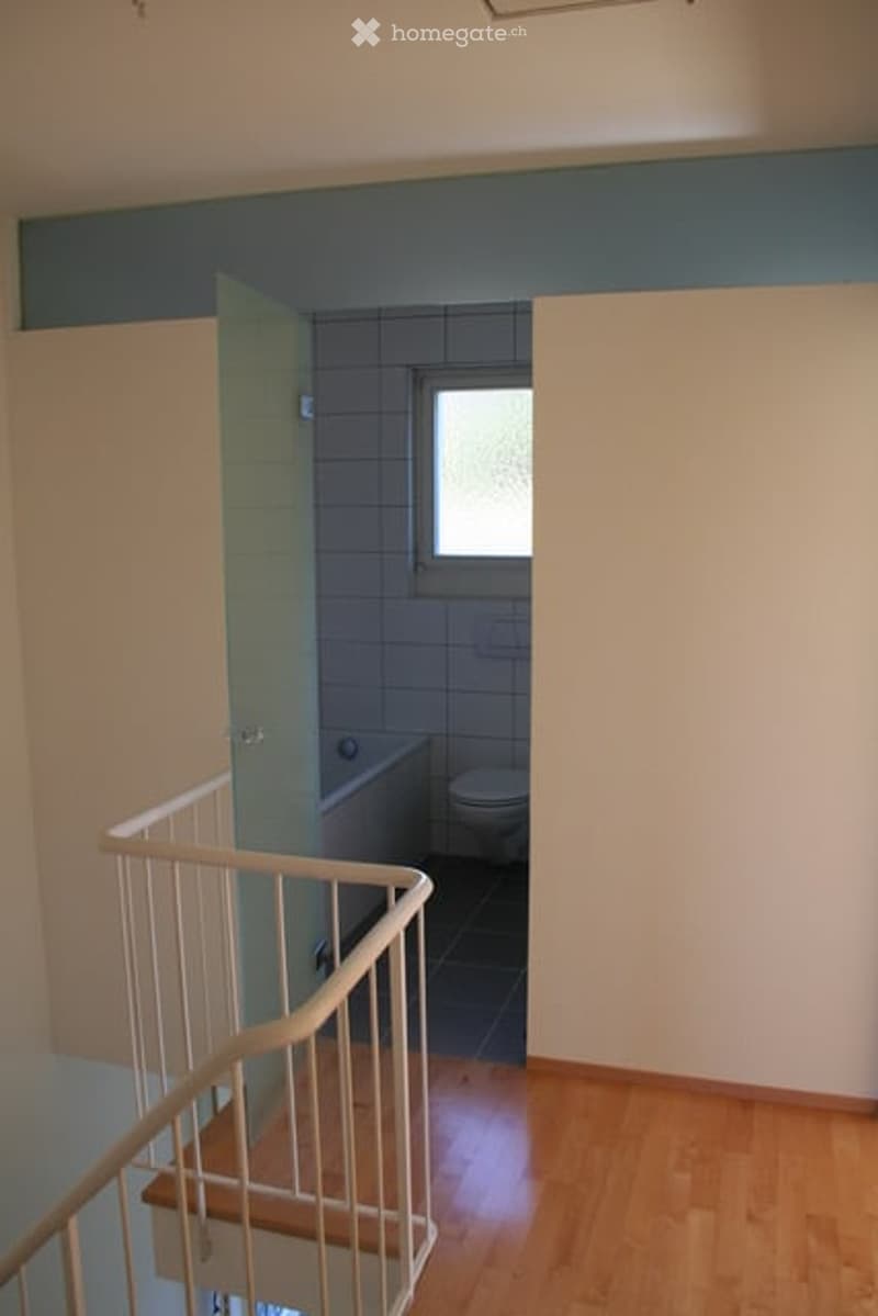 Empty room with wooden flooring, white walls, and a staircase leading to a bathroom area with a bathtub and toilet.