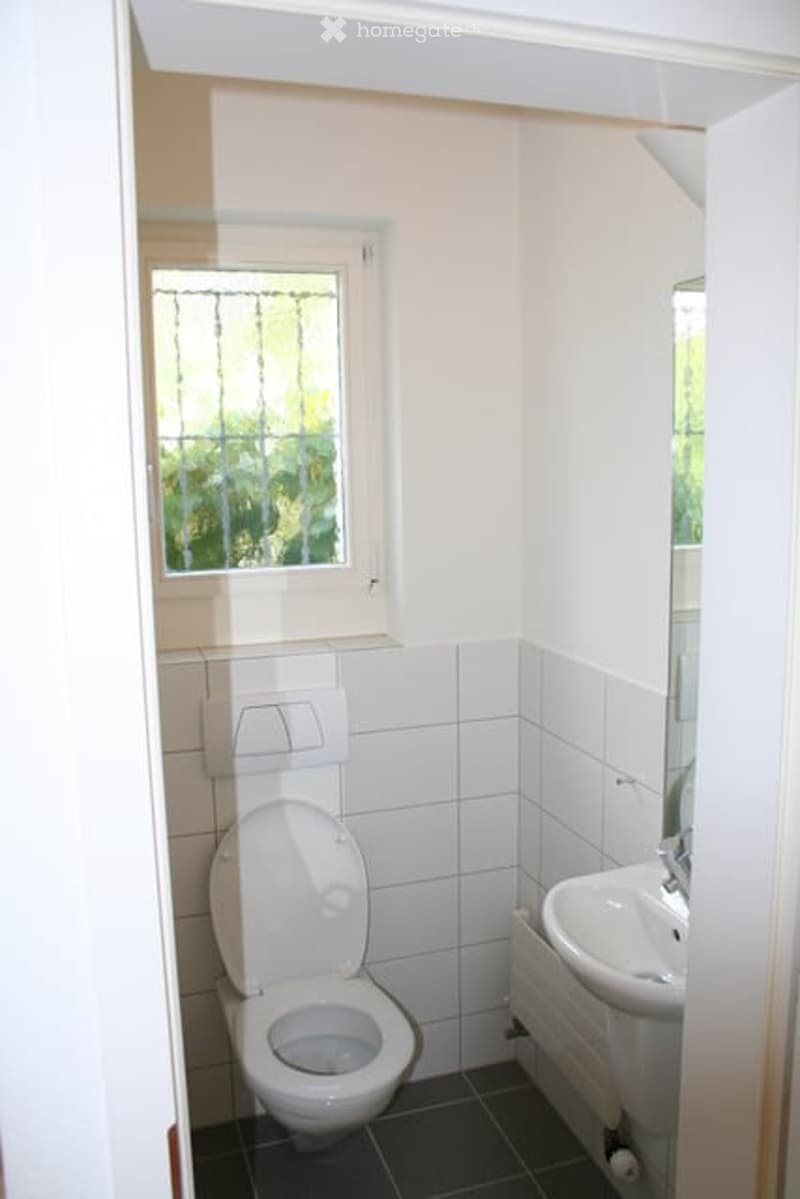 Small bathroom with white tiled walls, a toilet, a sink, and a window with frosted glass.