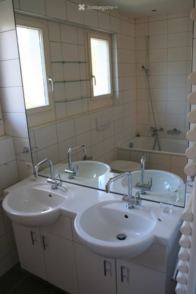 Modern bathroom with double sinks, large mirror, bathtub, and tiled walls.
