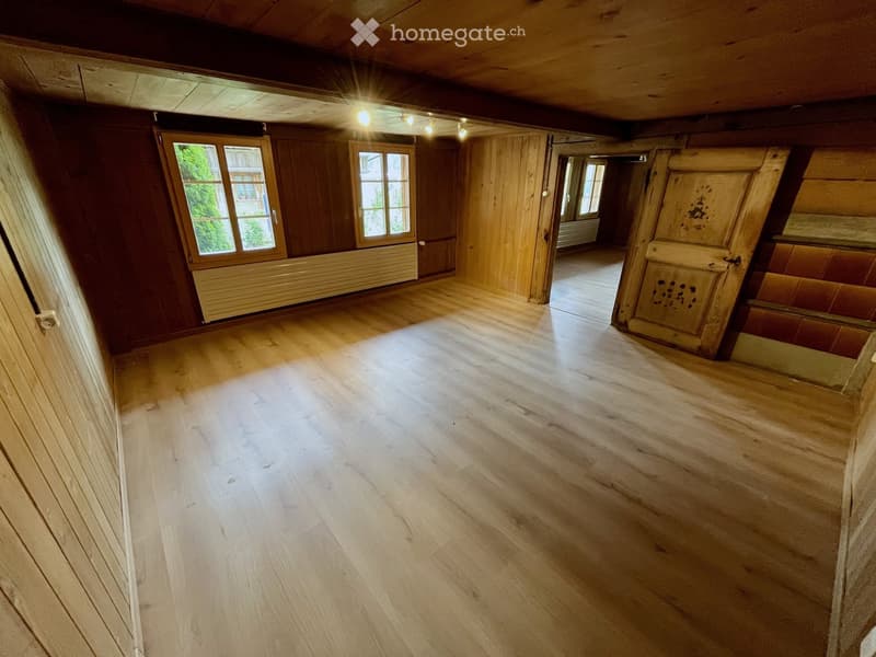 Empty room with wooden walls and floor, large windows, and exposed wooden beams on the ceiling.