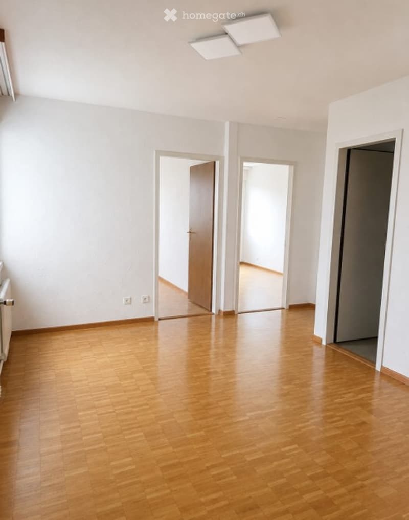 Empty room with wooden flooring, white walls, and multiple doors leading to other spaces.