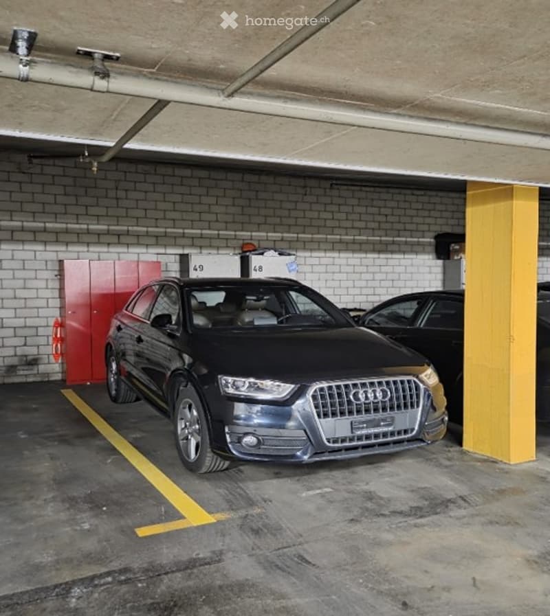 {"visible_features": ["Garage", "Parking place"], "type": "Garage", "objects": [], "description": "Underground parking garage with a black Audi parked in one of the designated spots. The garage features concrete floors, brick walls, and yellow painted par