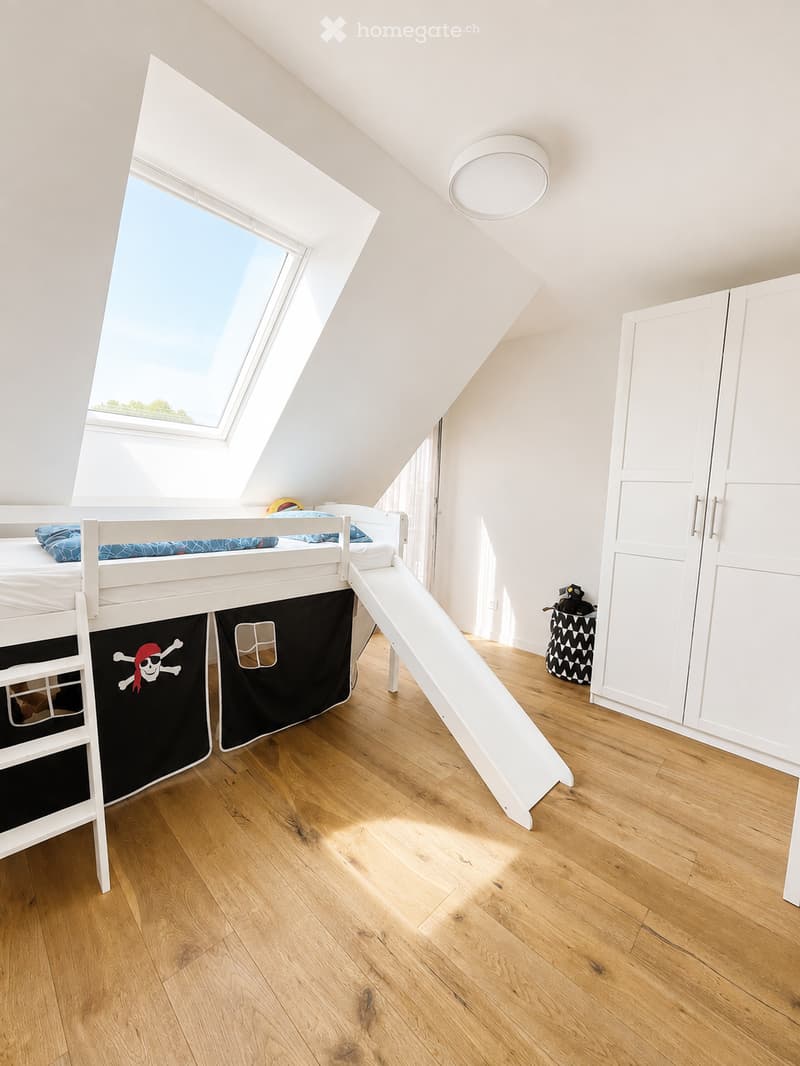 Bright attic bedroom with wooden floors, white bunk bed, slide, and large skylight window.