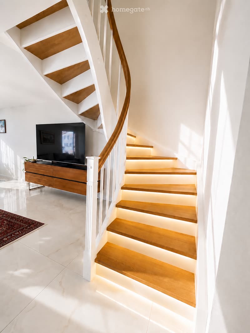 Spiral staircase with wooden steps and white walls, illuminated steps, television on wooden cabinet, small plant, and picture frame on wall.