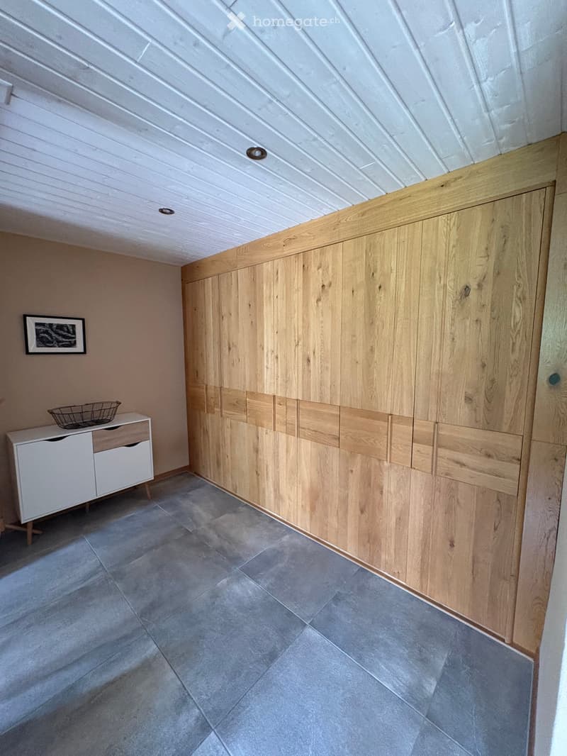 A modern hallway with wooden built-in cabinets, a white drawer unit, a small basket, and a picture frame on the wall.