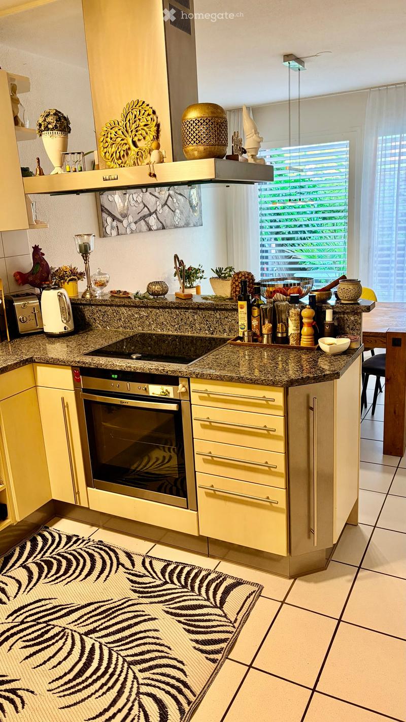 Modern kitchen with light yellow cabinets, granite countertop, stainless steel oven, and various appliances and decorative items on the counter.