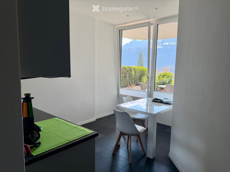 Dining area with a white table and chairs, a green placemat, a black countertop, a glass door leading to a balcony, and a view of the mountains