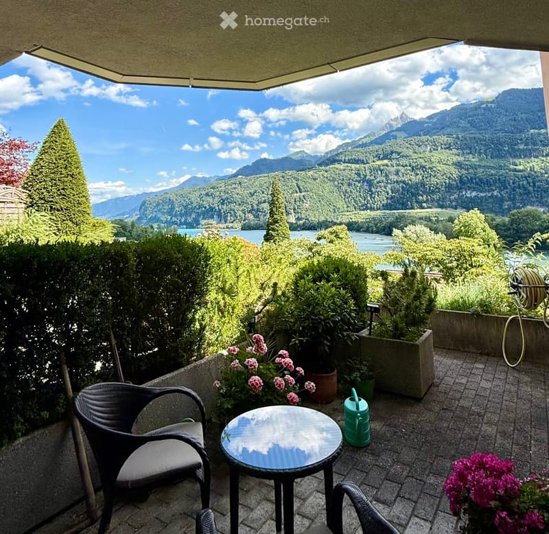 Balcony with a scenic mountain view, featuring a wicker chair, round table, and potted plants.