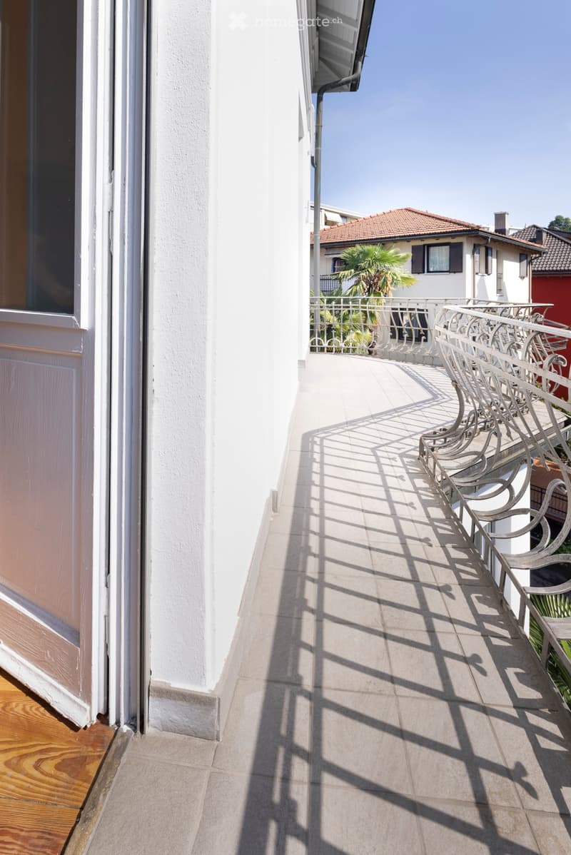 Balcony with tiled floor, white metal railing, and a view of neighboring buildings and greenery.