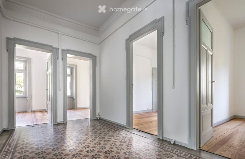 Empty hallway with white walls, wooden flooring, and multiple open doors leading to other rooms.