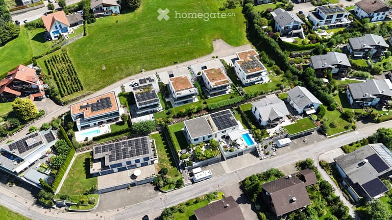Aerial view of a residential neighborhood with multiple houses, solar panels on roofs, and a swimming pool visible in one of the yards.