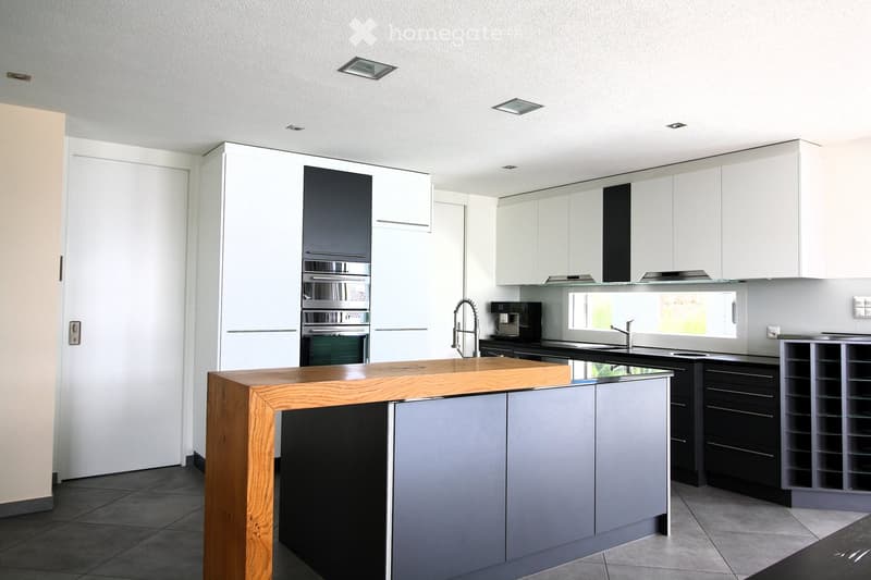 Modern kitchen with white and grey cabinets, a wooden island, stainless steel appliances, and a large window providing natural light.