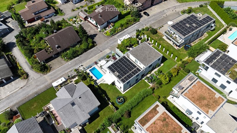 Aerial view of a residential neighborhood with multiple houses, solar panels, and a swimming pool.