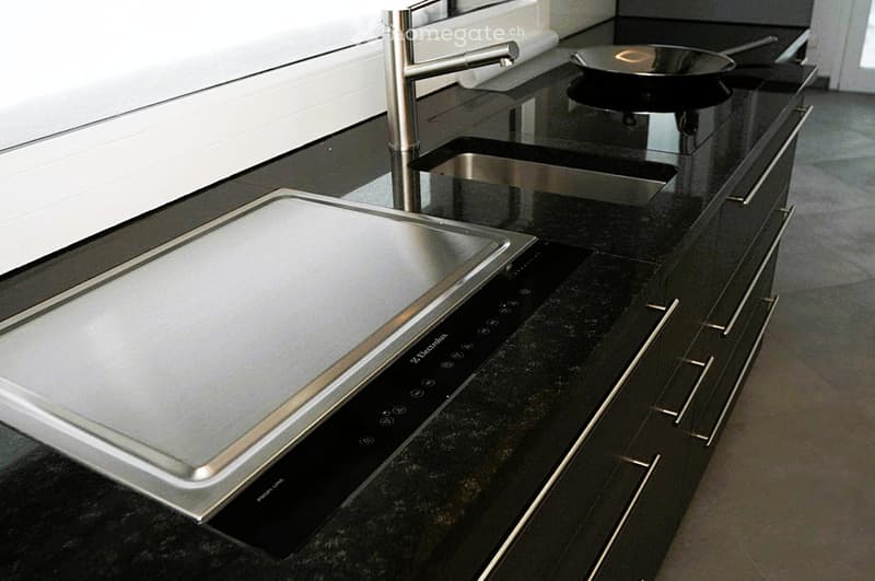 Modern kitchen with black granite countertops, stainless steel sink, induction cooktop, and a sleek faucet.