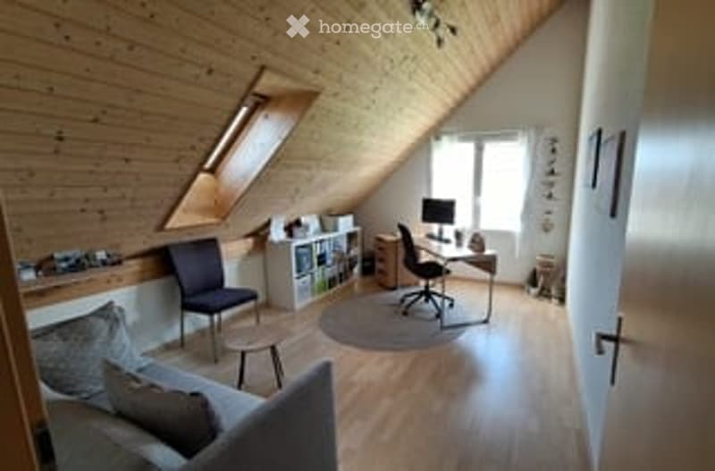 Bright, wooden-floored attic room with skylight window, modern furniture including a sofa, desk, and chair, and built-in shelving.