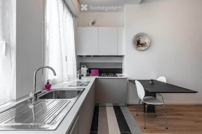 Modern kitchen with white cabinets, stainless steel sink, stove, and a small dining area with a table and chairs.