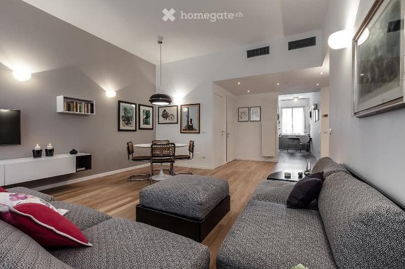 Modern living room with grey sofa, coffee table, dining table, chairs, TV, and decorative shelves.