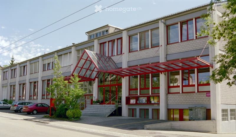 Multistory office building, white walls, red accents, multiple cars parked outside