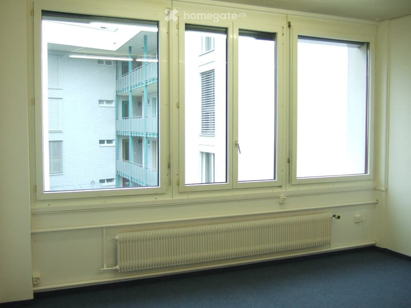 Empty room with large windows, radiator, and blue carpeted floor.