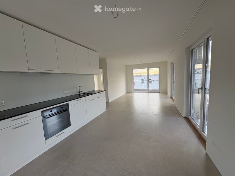 Modern kitchen with white cabinets, a sink, and an oven, connected to a spacious living area with large windows and sliding doors.