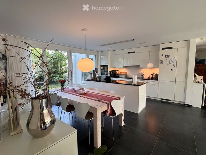 Modern kitchen with white cabinets, black countertops, a central island, a dining table with chairs, and a vase with branches on a side table.