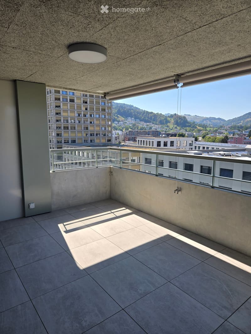 Modern balcony with tiled floor, glass railing, and a view of the city and surrounding hills.