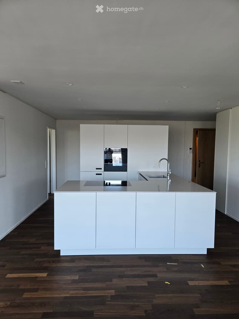 Modern kitchen with white cabinets, a central island, and a sink, featuring a dark wooden floor and recessed lighting.